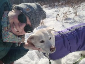 woman in sunglasses and little white dog taking selfie on a snowy trail