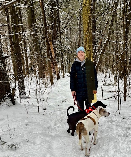person and two dogs on snowy hike. One dog is black and the other is white with brown spots