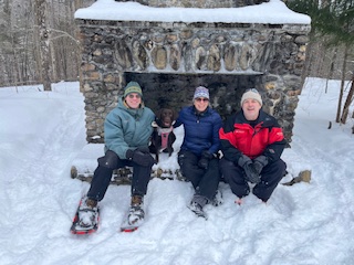 3 people with chocolate lab on snowy hike