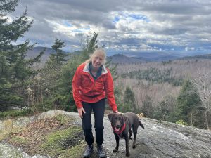 Woman in red jacket on mountain top during stick season with brown dog